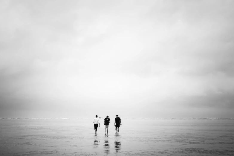 three people standing in the water on top of a beach