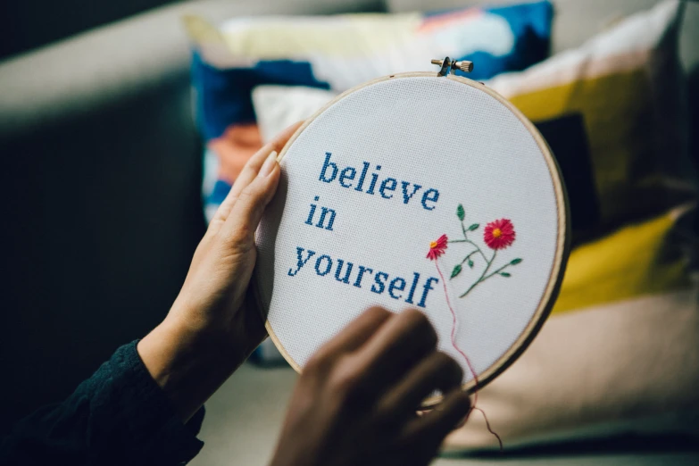 someone holding up a embroidery in front of a pillow with a saying