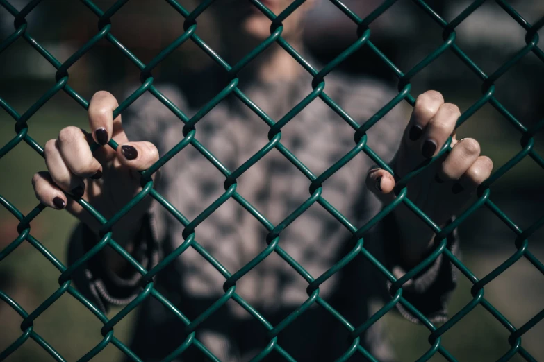 a woman behind a chain link fence with her hands outstretched