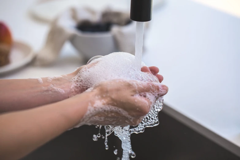 a woman washing her hands with soap from a kitchen sink faucet