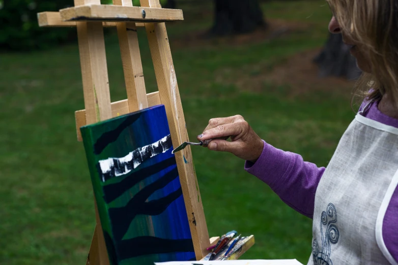 a woman painting on an easel in front of grass