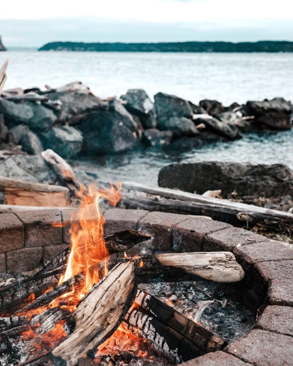 a bonfire is lit near some water on a shore