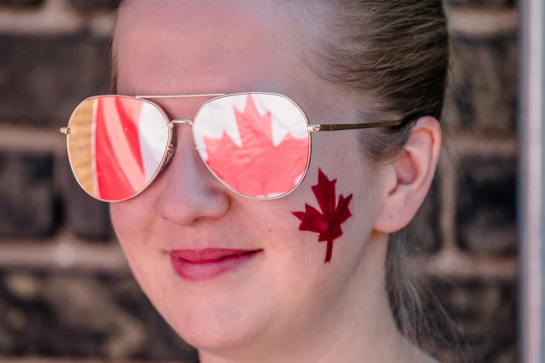 a woman wearing a pair of sun glasses has a maple leaf painted on her cheek