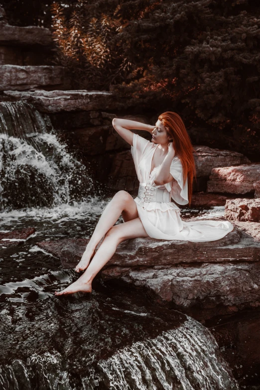 a woman wearing a white dress sitting on some rocks