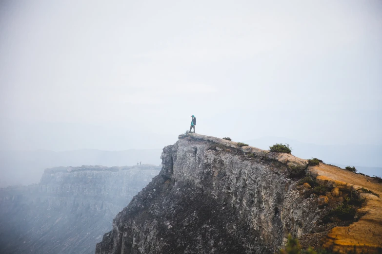 two people standing on top of a cliff with mountains in the background