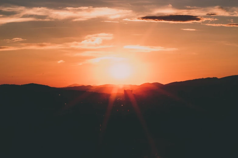 the sun shining in the distance with mountains and hills visible