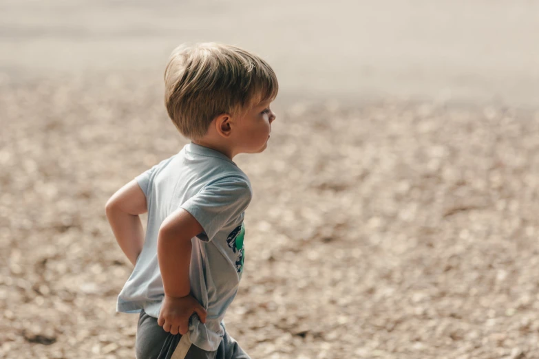 a little boy standing on the beach with his back turned