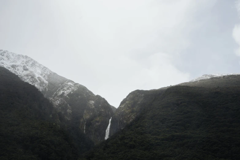 some trees and hills in front of snow covered mountains