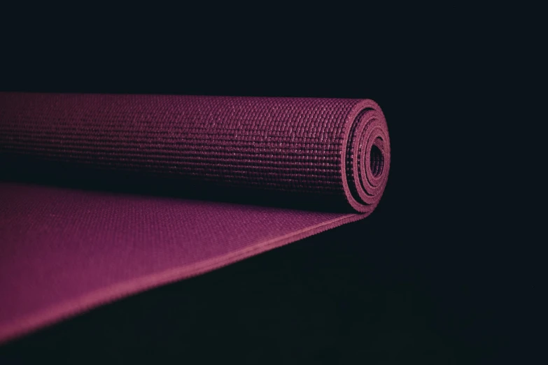 a purple yoga mat rolled up on a black surface
