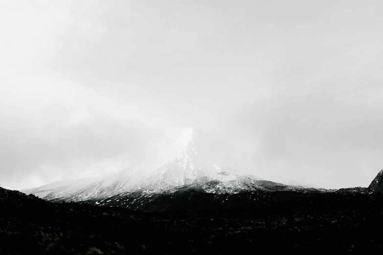 the peak of a snow - capped mountain rises toward a cloudy sky