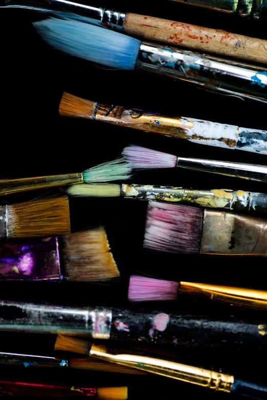 a number of paint brushes on a dark surface