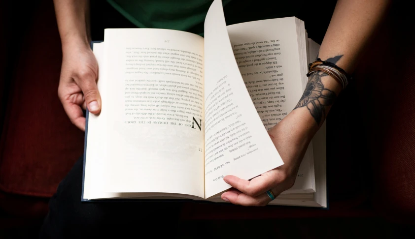 a person sitting on the couch holding a book with an open pages