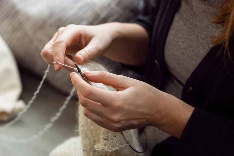 a woman sitting down and knitting a piece of fabric