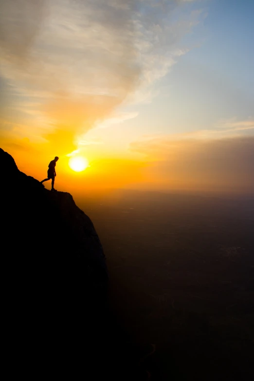 the sun is rising over the silhouette of a person on a cliff