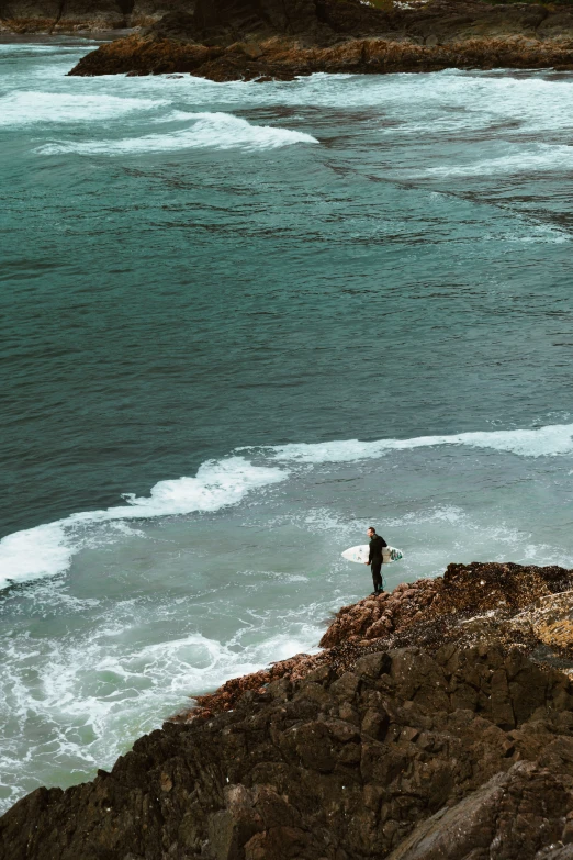 a man stands on the edge of a cliff overlooking the water