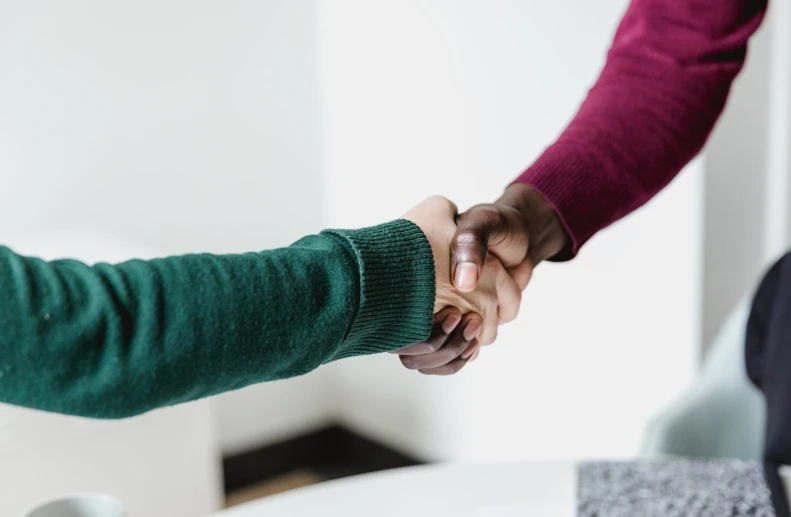 two people standing close together, one holding hands and the other wearing a maroon sweater