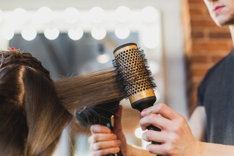 a hair stylist blow drying a woman's long hair