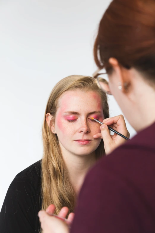 woman with pink face paint is getting ready to use the make up