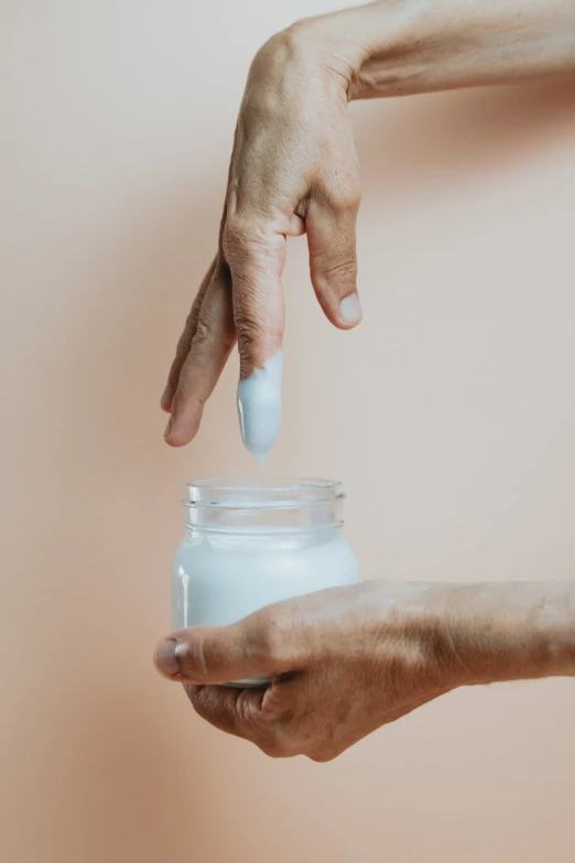 two hands reaching for a small jar with white paint