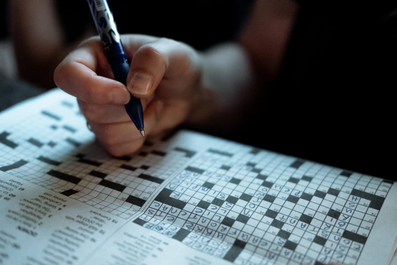 a person with their hand on the crossword puzzle paper