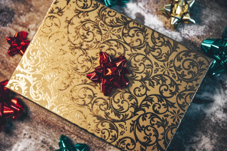 a gold gift box with red bow sitting on top of it