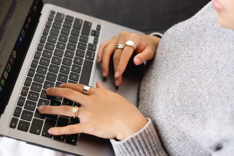 two hands are on a keyboard and two rings are on the finger of the person who is holding the phone