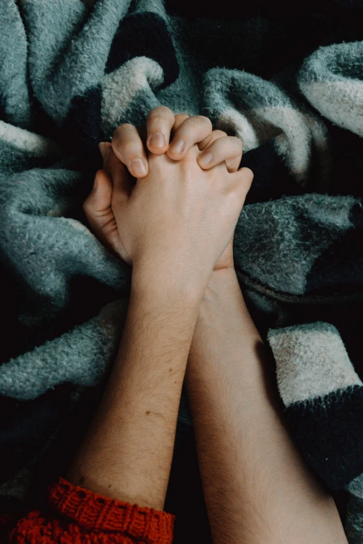 a couple of hands on a grey blanket together