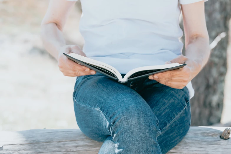 a person sits on a log with a book in their hands
