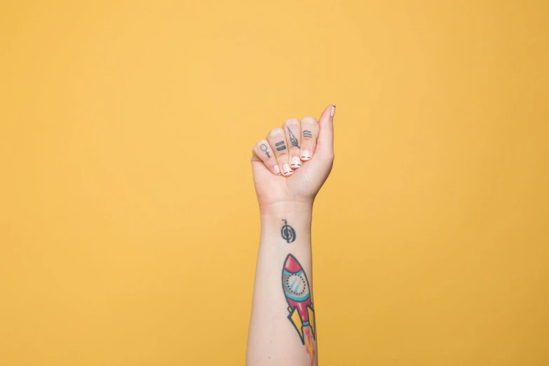 the small arm with tattoos holds out one finger and an arm pin