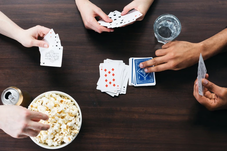 three people that are playing card games with a bowl of popcorn