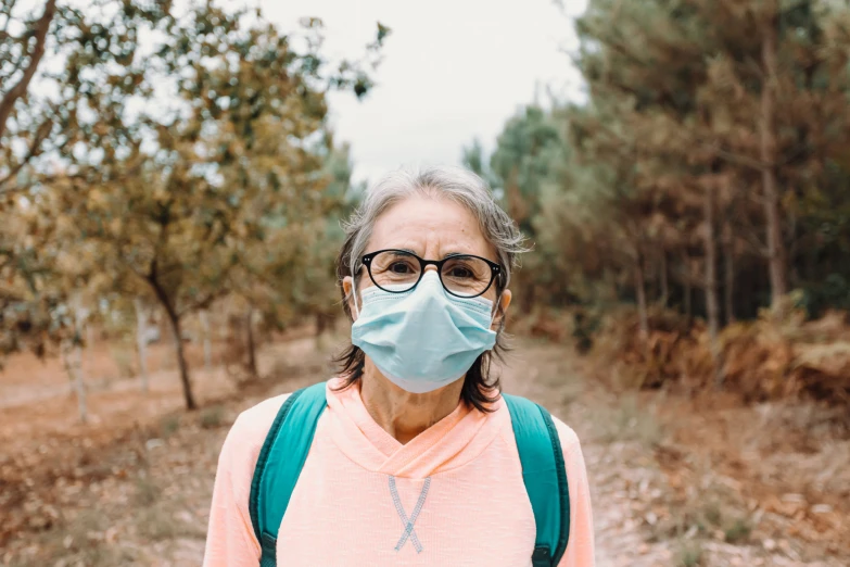 an old lady wearing a protective face mask while standing on a dirt road