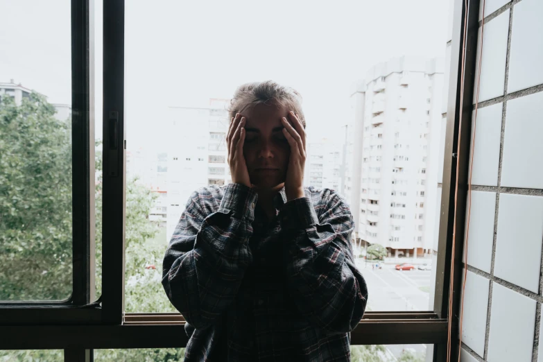 a woman holding her head next to a window