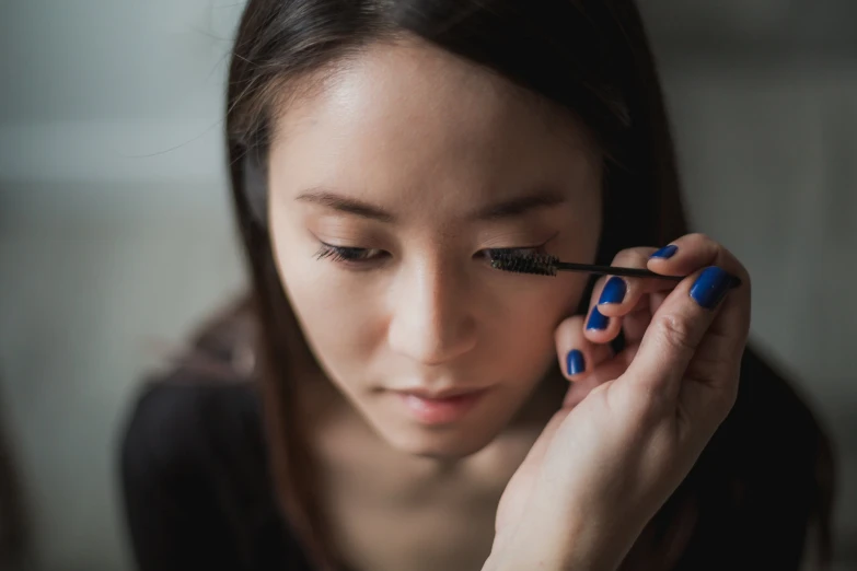 a woman with blue fingernails using a mascara