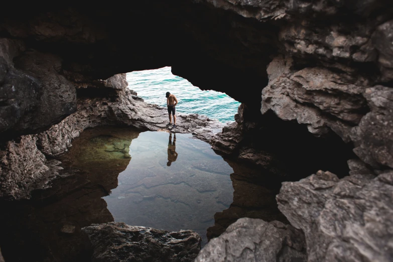 person looking into the water near a cave