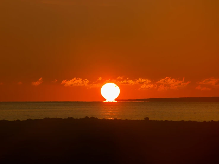 a very bright orange sunset behind a calm ocean