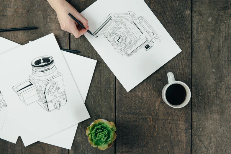 two drawings are on a table next to a cup and pen