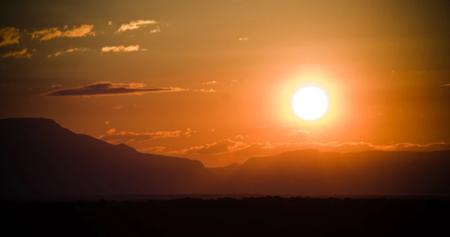 a bright sun is setting on a cloudy sky