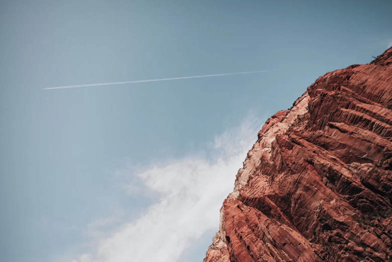 an airplane flying over red mountain and white clouds