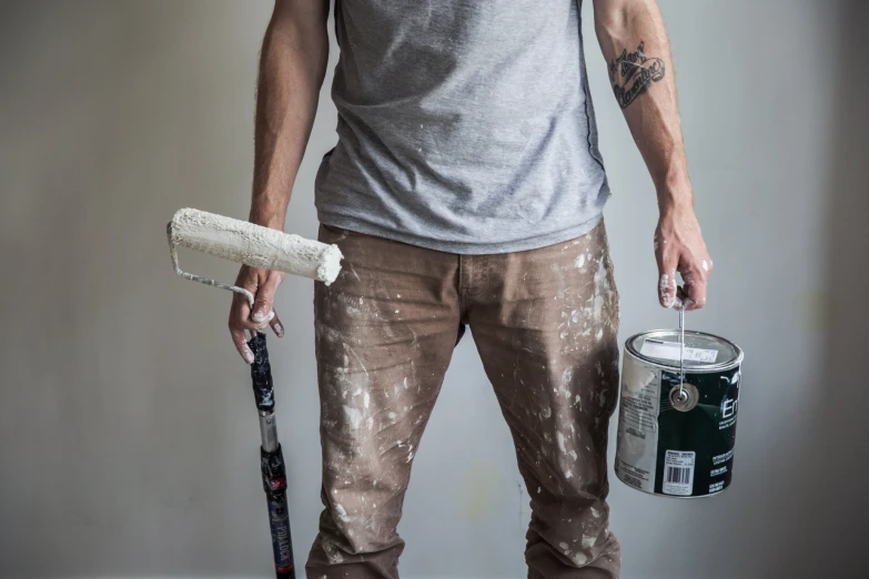 a man holding a paint roller, a white can and a brush