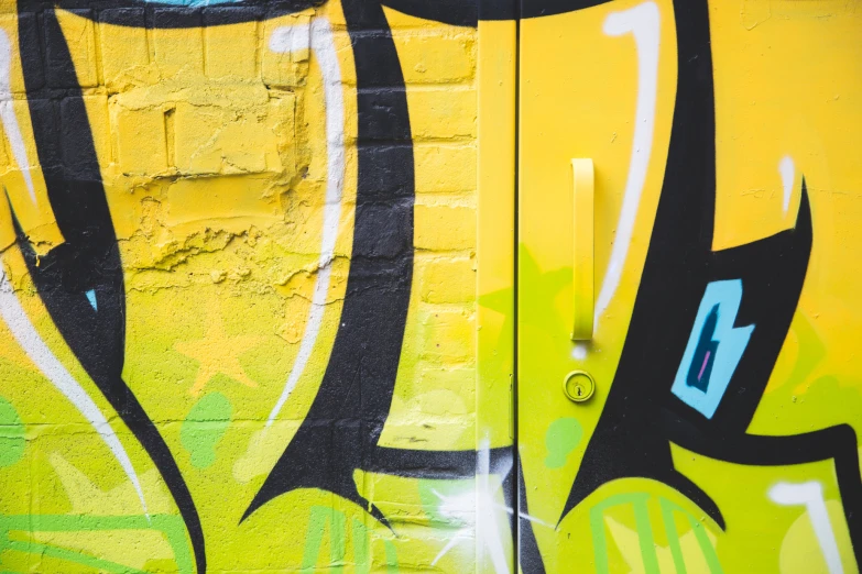 a wall with yellow and black graffiti and a door that has a metal lock