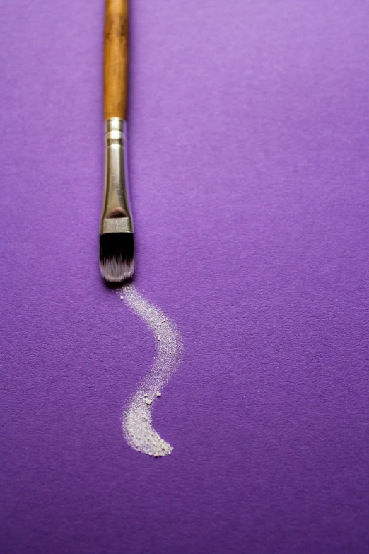 an angled view of a paint brush with white powder on a purple surface