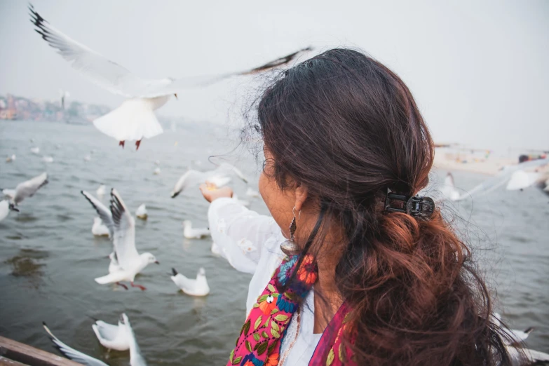 a woman looks out at a seagull flock as she stands on a dock