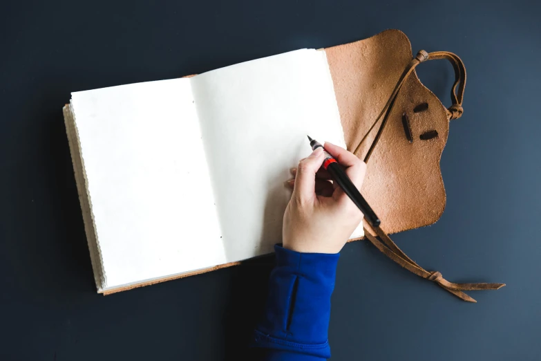 a hand holding a pen writing on an open notebook