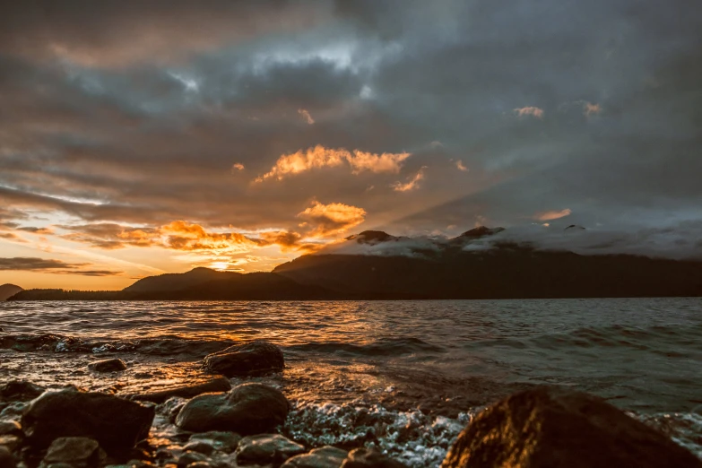 a sunset seen over the water on a rocky beach