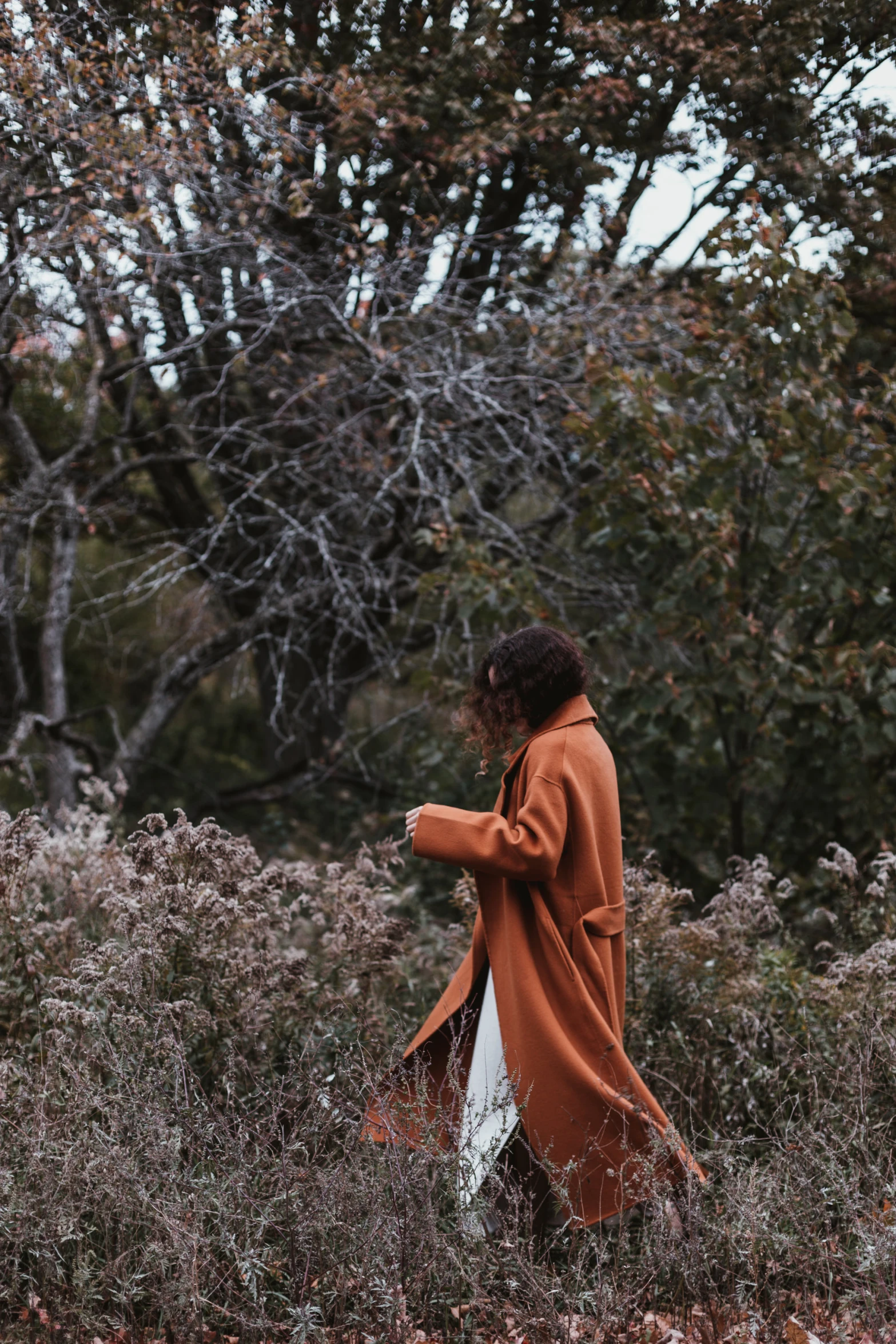 a woman in an orange coat is walking through the woods