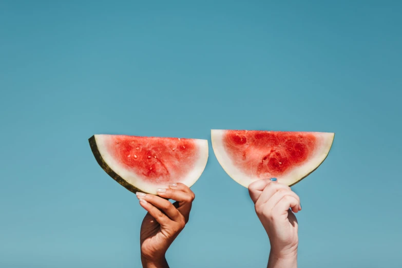 two people holding slices of watermelon on a blue sky