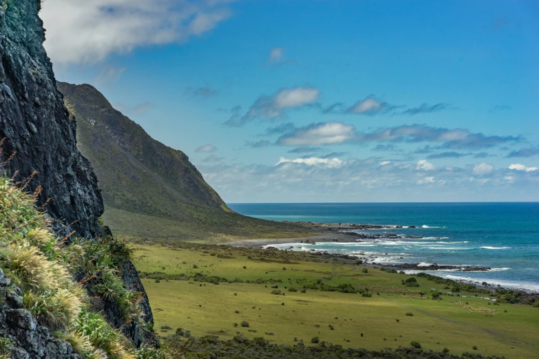 the side of a mountain overlooking the ocean with grass and rock formations