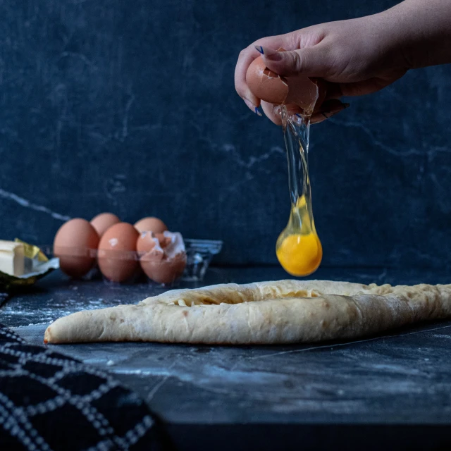 person preparing fresh bread at dark table next to eggs