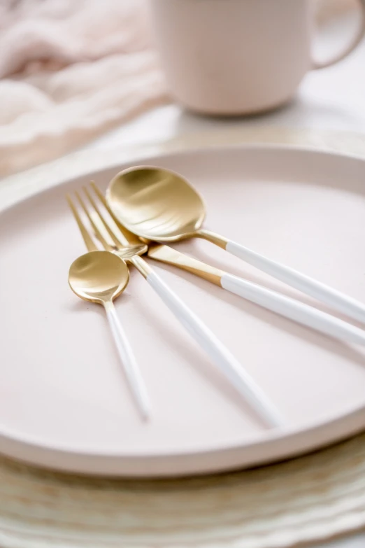 a white plate topped with gold spoons next to a white cup