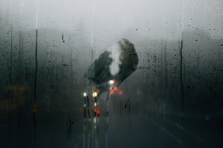 rain falls on a windshield as a cyclist in black stands beside a building